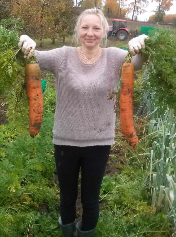 Emilia Mikulewicz proudly holding two large harvested carrots on family farm in Poland, reflecting her early hands-on experience in crop cultivation and practical agricultural work during her formative years.
