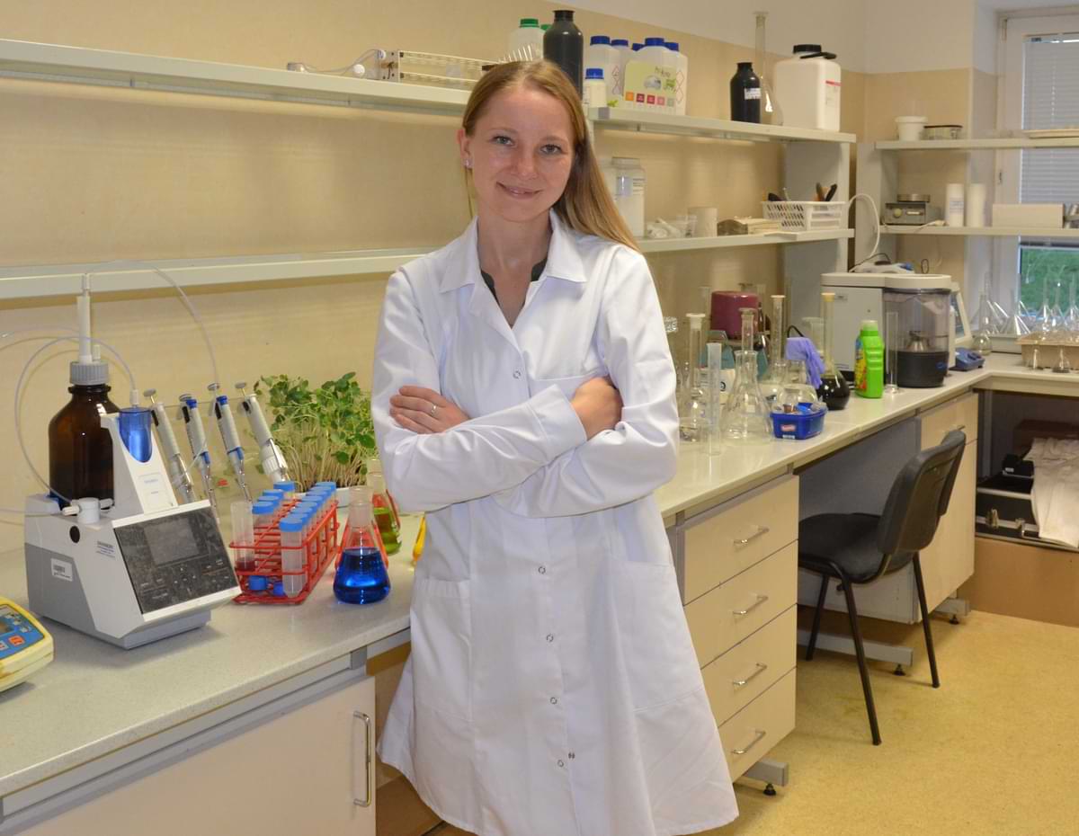 Dr. Emilia Mikulewicz in a laboratory setting, wearing a white lab coat, surrounded by scientific equipment and plant samples, highlighting her academic background and research in agronomy.
